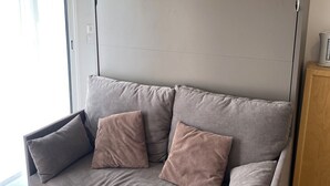 Een moderne woonkamer met een grijze bank, twee gestreepte kussens, een witte salontafel en een houten kast.