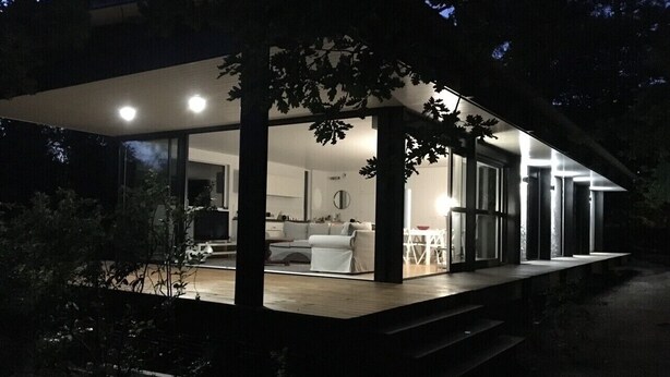 Une maison moderne dotée d’un patio couvert, d’un salon visible avec un canapé et une table basse, et d’une cuisine en arrière-plan.