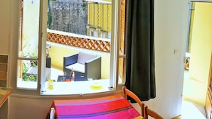 Et værelse med et vindue der viser en balkon med orange gelændere, en flisebeklædt væg og en trædør.