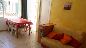 Et værelse med spisebord og stole, en sofa med hynder, en dør og et vindue med udsigt.