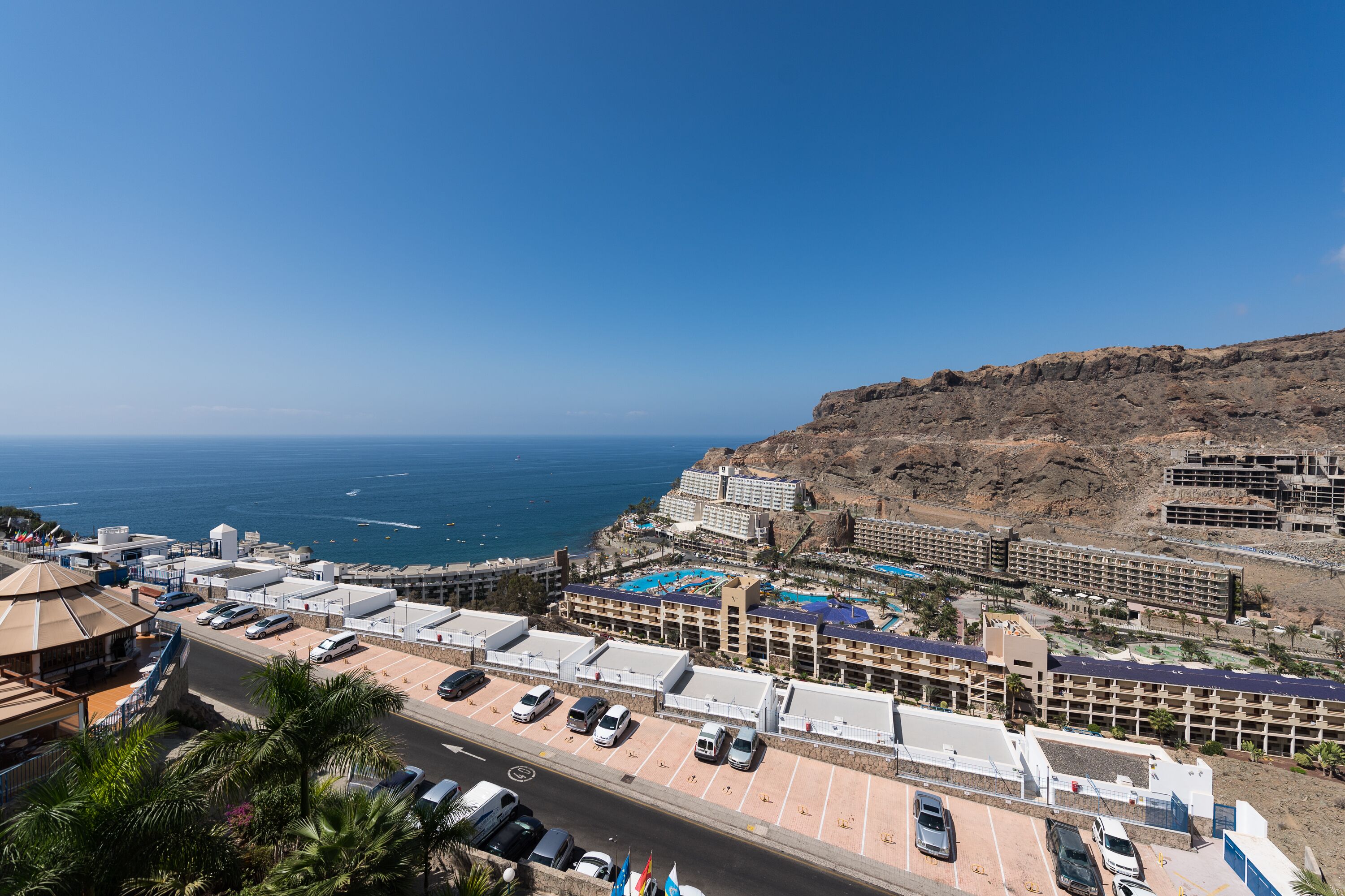 A coastal hotel with multiple buildings, a parking lot, and a view of the ocean.