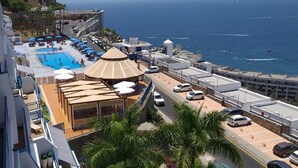 A rooftop pool area with a large pool, sun loungers, and umbrellas, overlooking a coastal cityscape. - Apartment with terrace to enjoy beautiful views. (Mogán)
