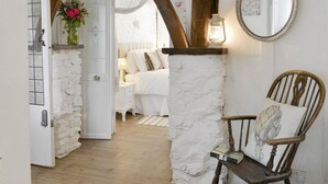 A cozy bedroom with a stone wall, a wooden chair, a bedside table, and a mirror.