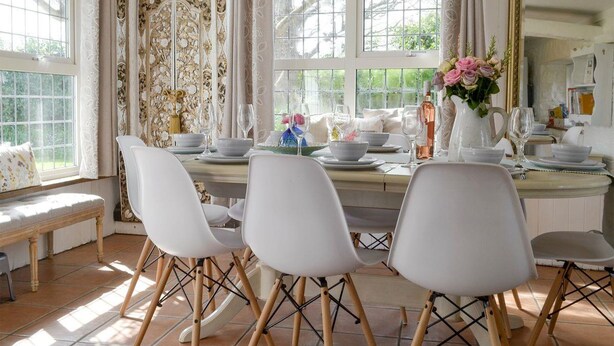 A dining area with a white table set for four, surrounded by white chairs with wooden legs.
