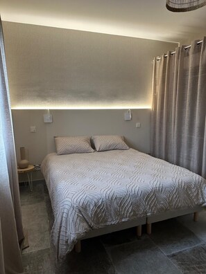 Ein Schlafzimmer mit einem Bett, einem Nachttisch, einer Lampe und einem Vorhang.
