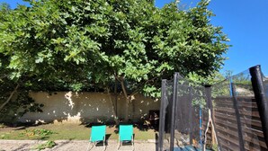 A fenced outdoor area with two green chairs, a trampoline, and a tree providing shade. - The house patio of Velleron (Velleron)