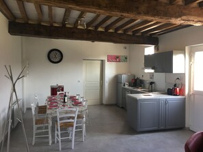 A dining area with a table set for four, a kitchen with grey cabinets, and a wooden ceiling. - cozy cottage ideal for quiet family holiday (Moyaux)