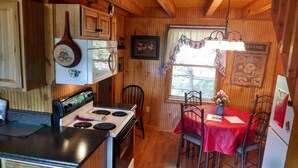 Una cocina compacta con estufa, una mesa de comedor con sillas, paredes de madera y una ventana con persianas.