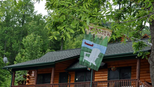 Una cabaña de troncos con un balcón y un cartel que dice "Bienvenido".