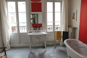 Un baño con lavamanos blanco, bañera y ventana con vistas a un balcón.