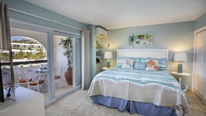 A bedroom with a bed, a sliding glass door leading to a balcony, a small table with chairs, and a potted plant.