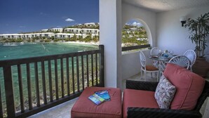 A balcony with a view of the ocean and a resort area. There is a table with chairs and a plant.