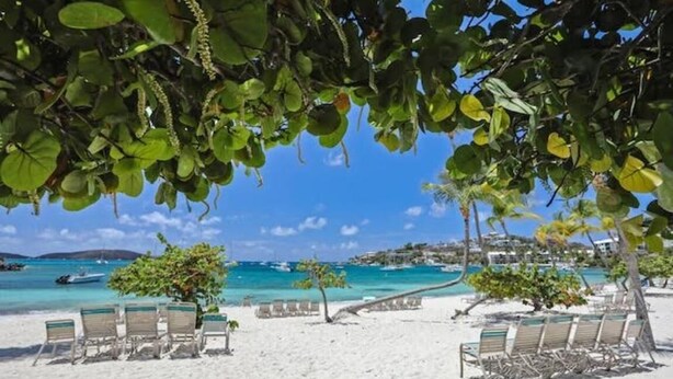 A beach with white sand, lounge chairs, and a view of the sea.