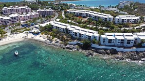 A coastal resort with multiple white buildings, clear turquoise waters, and a sandy beach.