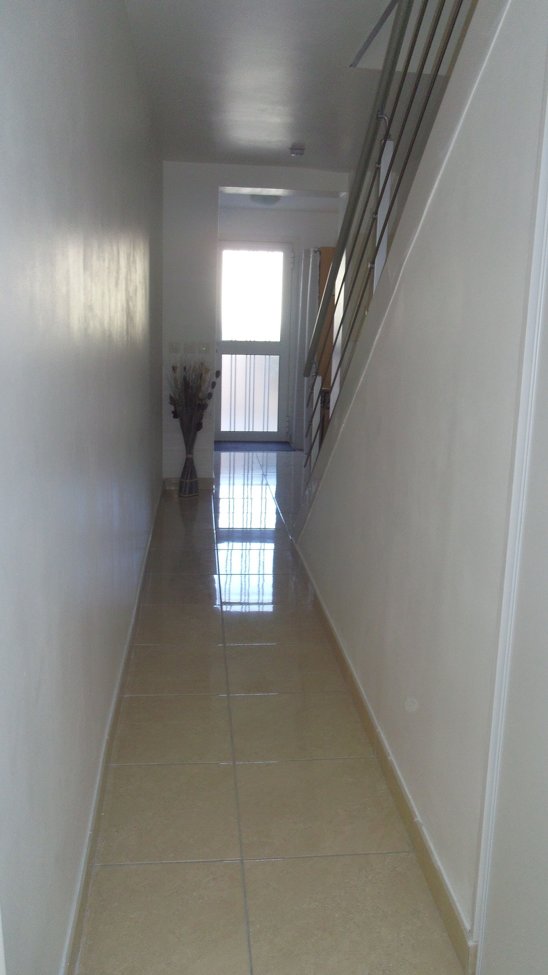 Un estrecho pasillo con baldosas, una escalera a la derecha y una puerta al final.