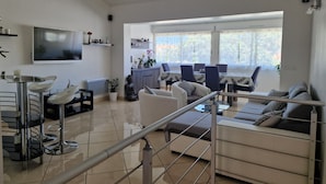 En moderne stue med et fladskærms-tv, et spiseområde med bord og stole, og en trappe med gelænder.
