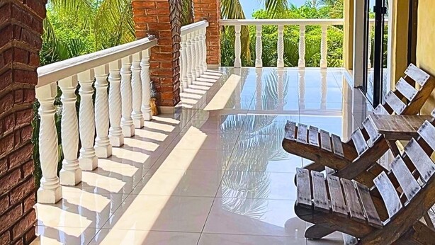 Un espace extérieur abrité, doté d’un sol carrelé, de balustrades blanches et offrant une vue sur des palmiers.