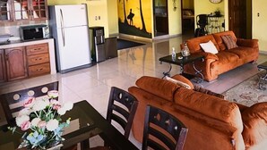 Un grand espace de vie comprenant un canapé, une table à manger et des chaises. On y trouve également des ventilateurs de plafond, un réfrigérateur et un coin cuisine avec des placards et un four à micro-ondes.