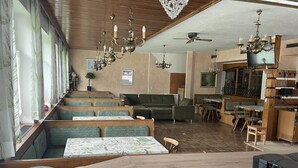 A restaurant with wooden tables, green cushioned seating, chandeliers, and a ceiling fan.