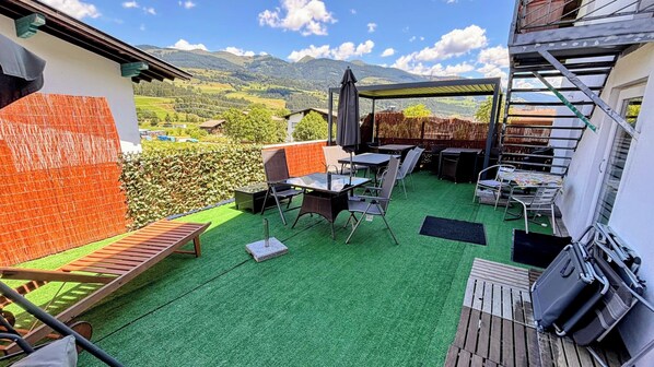 A rooftop terrace with a view of mountains, a barbecue area, and outdoor seating.
