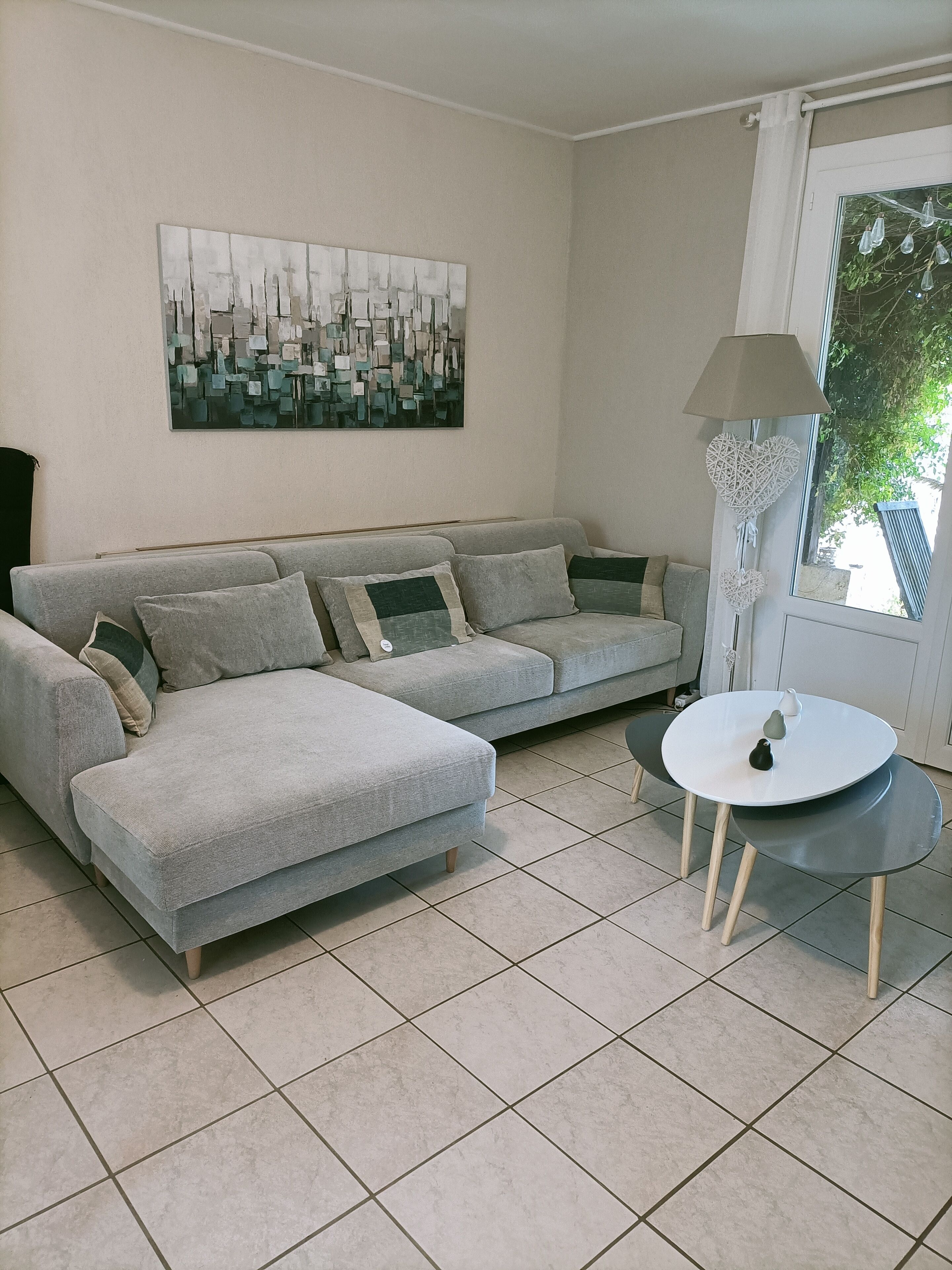 A living room with a grey sofa, a white table, and a cityscape painting on the wall.