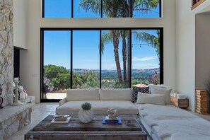 A modern living room with a large window, a stone fireplace, a white sofa, and a wooden coffee table.