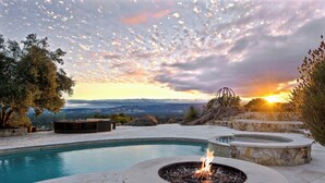 Una piscina amb una zona de foc, seients de pedra i vista al capvespre.
