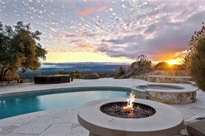 A pool with a fire pit, stone seating, and a view of the sunset.