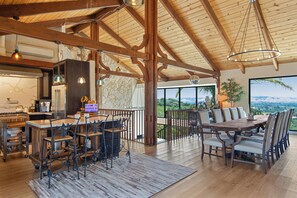 A spacious dining area with a large wooden table and chairs, a kitchen with marble countertops, and a view of the landscape through large windows. - Stunning Private Wine Country Estate - Epic Views - Pool - Hot Tub - Sunsets! (Sonoma)