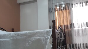 Een slaapkamer met een bed, een raam met gordijnen en een betegelde vloer.