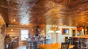Un interior rústico con paredes de madera, una zona de bar y un espacio de comedor con mesas y sillas de madera.