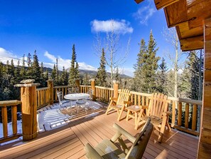 A wooden deck with a table and chairs, overlooking a snowy mountain and forest.