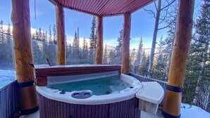 Un jacuzzi en un gazebo de madera con vista a un bosque nevado.