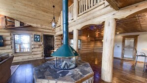 Interior de una cabaña de troncos con chimenea de piedra, pisos de madera y un balcón.