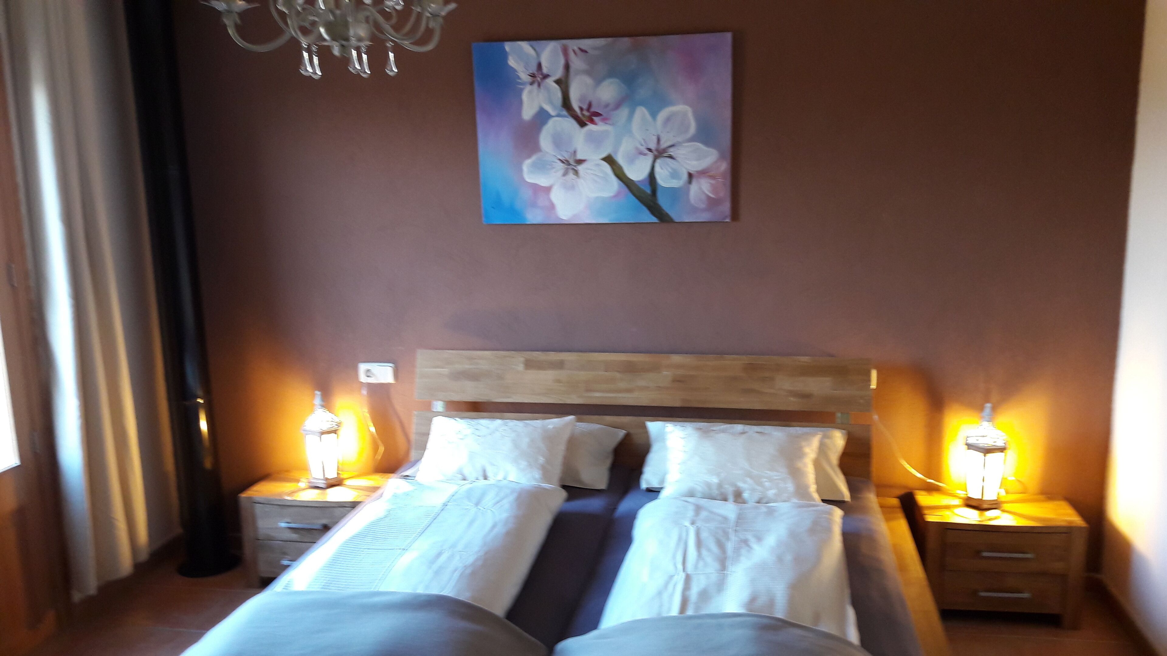 A double bed with white linens, two bedside tables with lamps, a wooden headboard, and a wall-mounted painting of flowers.
