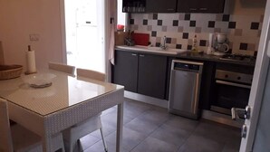A modern kitchen with a dining table, dark cabinets, a dishwasher, and a coffee maker. - Very well equipped apartment, 2 bedrooms, living room, guarded parking (EL AOUINA)