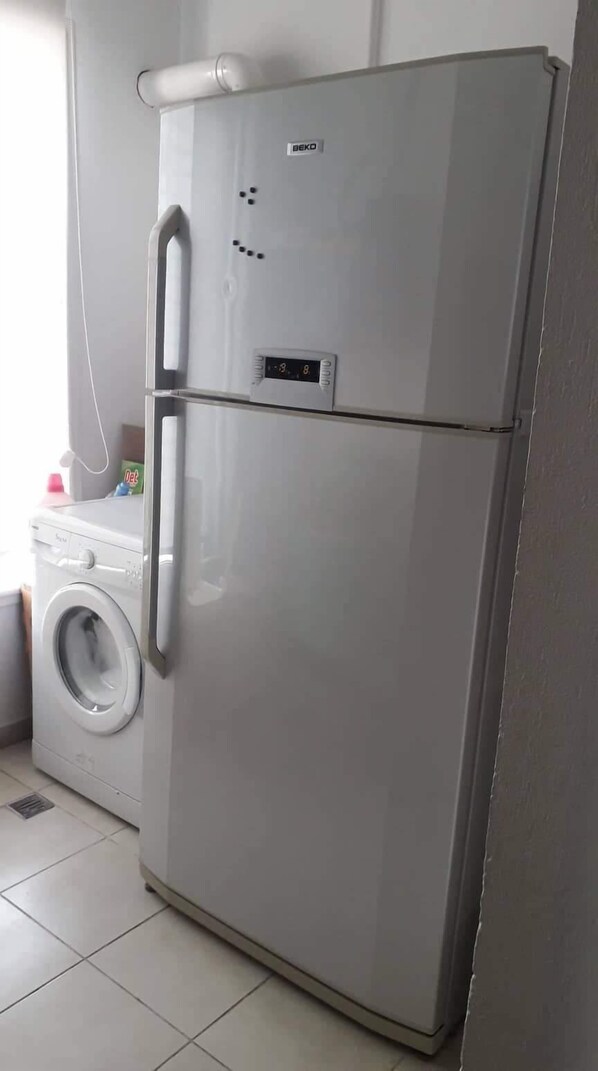 A compact, two-door refrigerator with a digital display, situated in a kitchen with a washing machine nearby. - Very well equipped apartment, 2 bedrooms, living room, guarded parking (EL AOUINA)