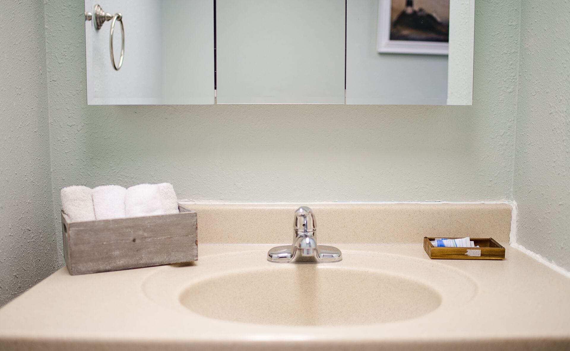 A bathroom sink with a mirror above it, a towel rack, and a small wooden box with a tissue box.
