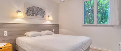 A bedroom with a bed, bedside tables, a wall-mounted light fixture, a window with curtains, and a wall art piece.