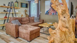 Una sala de estar con un sofá modular, una mesa de centro de madera, una estantería escalonada y una gran escultura de madera.