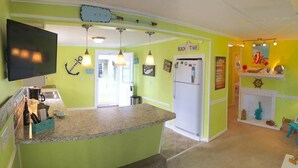 A kitchen with a TV, a refrigerator, and a counter. There are hanging lights and a sign that says "Beach Time".