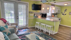 A living room with a sofa, a coffee table, and a kitchen area with a bar stool.