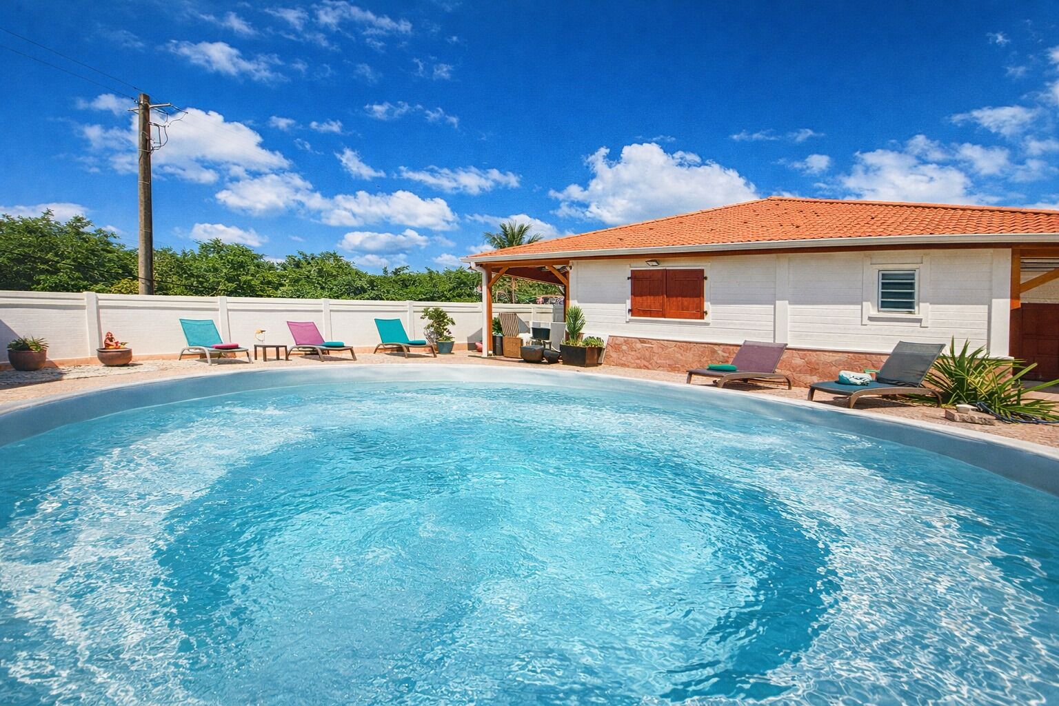 A swimming pool with lounge chairs, a covered patio, and a white building with a red roof.