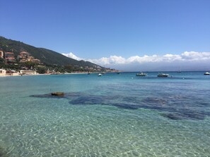 A coastal scene with clear turquoise water, boats, and buildings on a hillside.