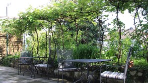 An outdoor patio with metal chairs and a table, surrounded by greenery and a stone wall. - Sunny apartment in an ideal location to Lake Kaltern, historic village (Kaltern)