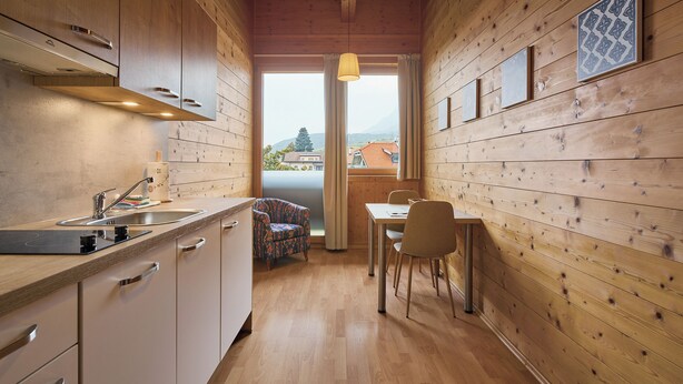 A compact kitchen with wooden walls, a dining area with a table and chairs, and a view of a mountain through a large window. - Sunny apartment in an ideal location to Lake Kaltern, historic village (Kaltern)
