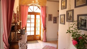 Une pièce avec une porte en bois, des rideaux roses, un lustre et des tableaux encadrés accrochés au mur.
