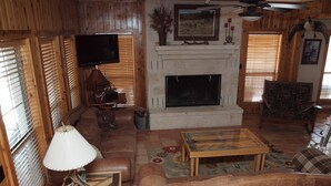 A cozy living room with a fireplace, wooden furniture, and a television. - Hill Country Getaway with great views (Mountain Home)