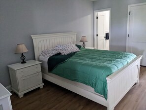 A bedroom with a white bed, green bedding, two bedside tables with lamps, a white dresser, and a door. - 2 BR Bayfront Condo with Gorgeous Sunsets, in Ocean City NJ (Ocean City)