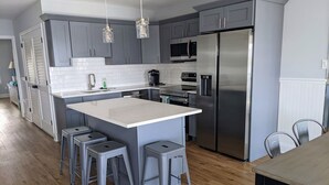 A modern kitchen with grey cabinets, a stainless steel refrigerator, and a central island with bar stools. - 2 BR Bayfront Condo with Gorgeous Sunsets, in Ocean City NJ (Ocean City)